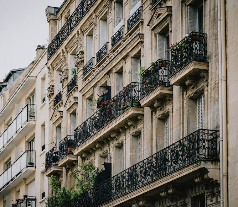 Façade d’immeuble parisien en pierre de taille, balcons en fer forgé et fenêtres à volets